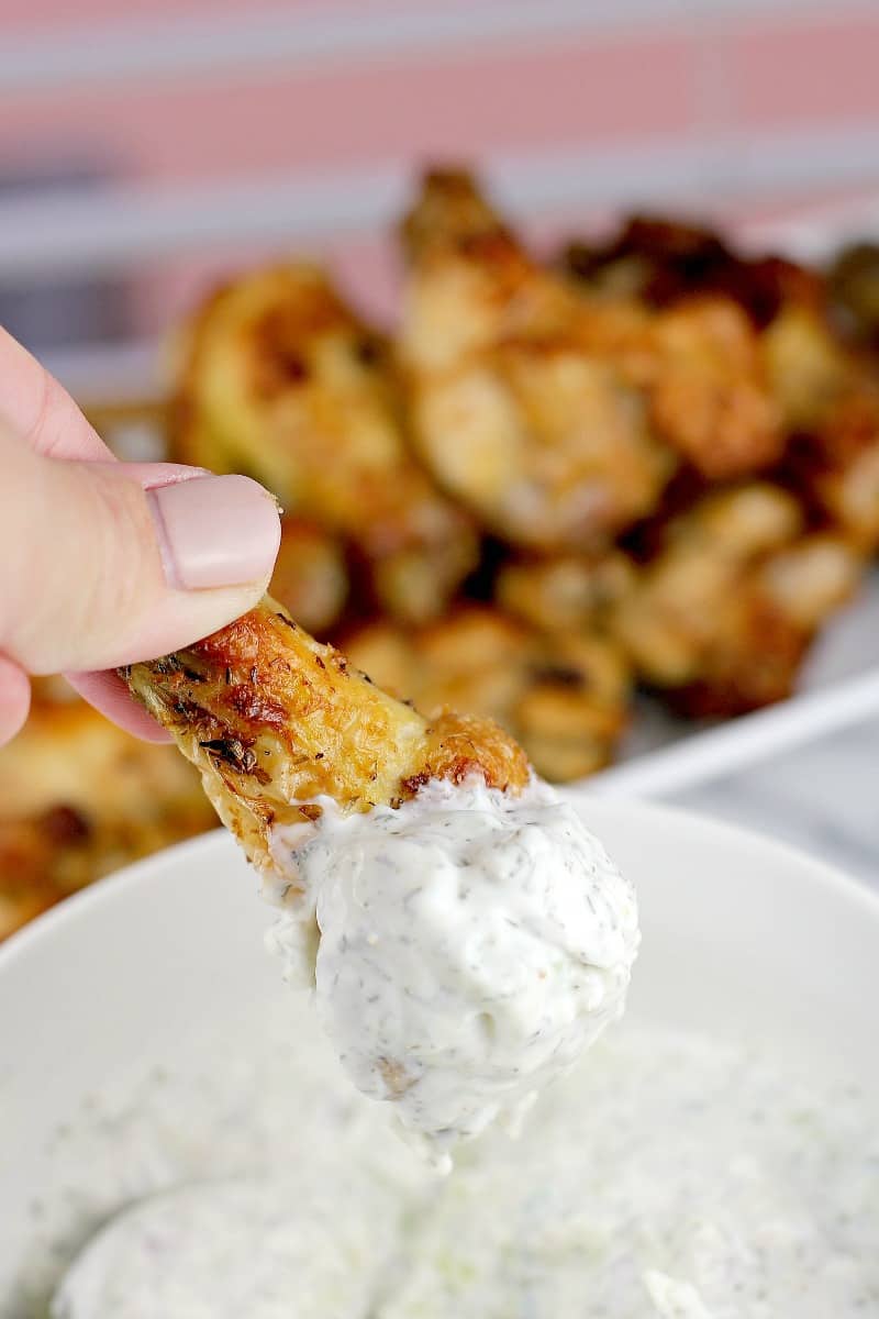 hand holding a Greek-Style Air Fryer Chicken Wing dipped in tzatziki sauce