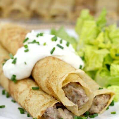 beef stroganoff crepes on a dish, topped with sour cream with a side of salad