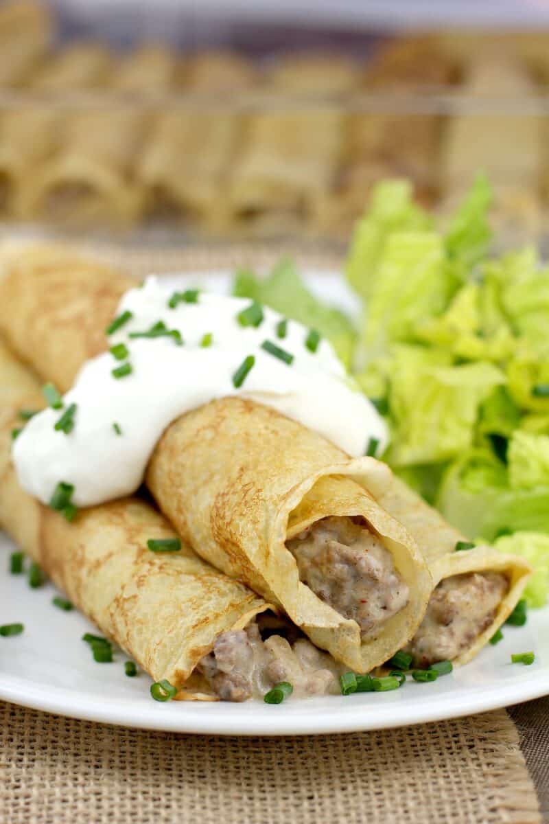 beef stroganoff crepes on a dish, topped with sour cream with a side of salad