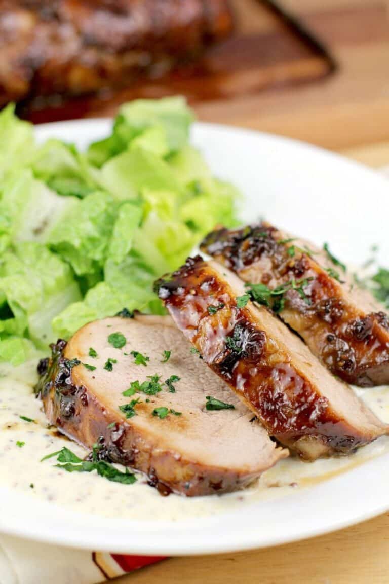 sliced pork medallions with bourbon glaze, on white serving plate with salad
