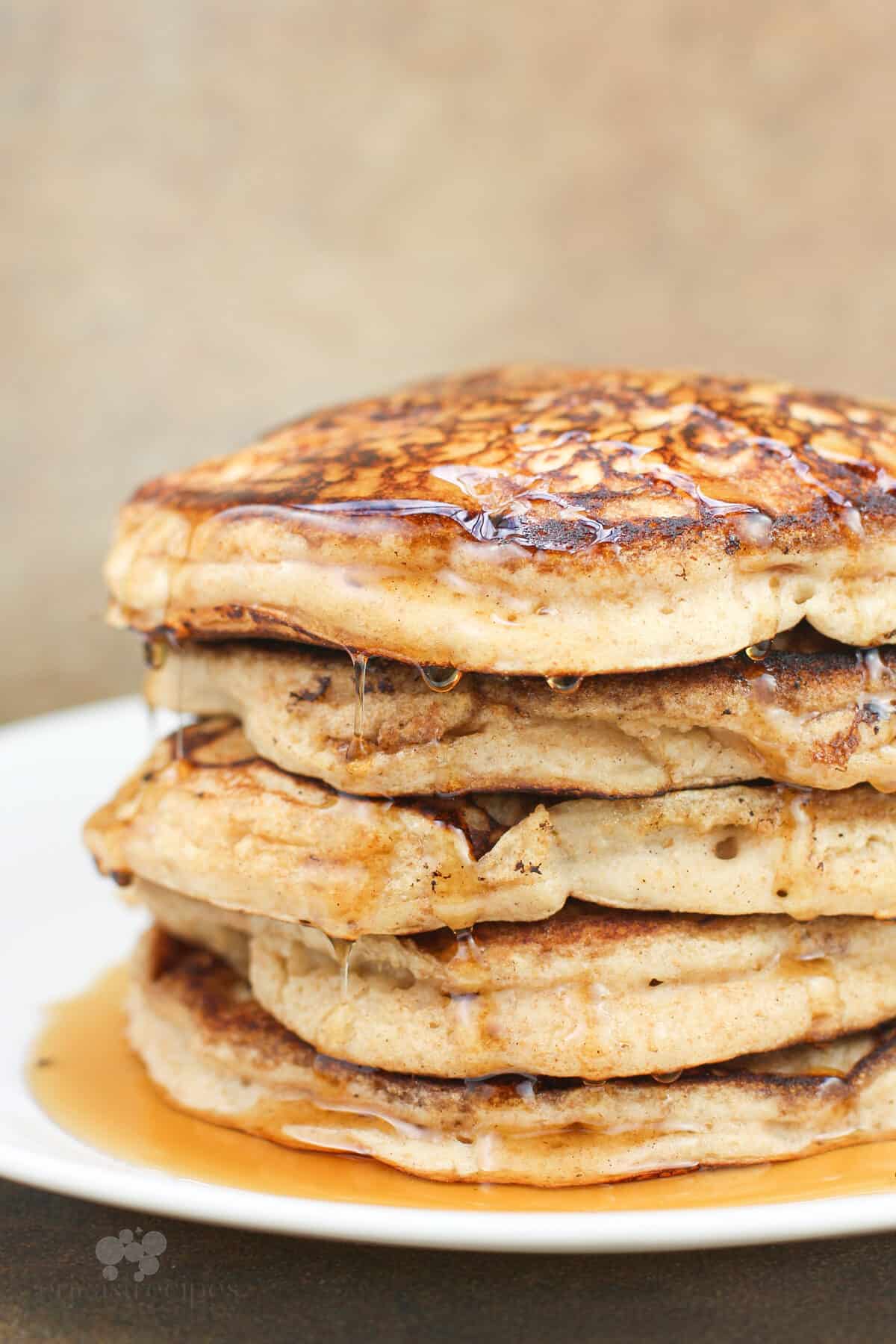 pancakes dripping with syrup stacked on white plate, side view
