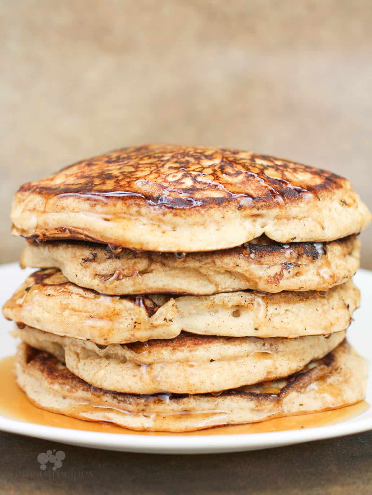 pancakes dripping with syrup stacked on white plate, side view