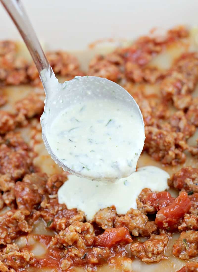 white ricotta herb sauce being ladled on a layer of meat sauce