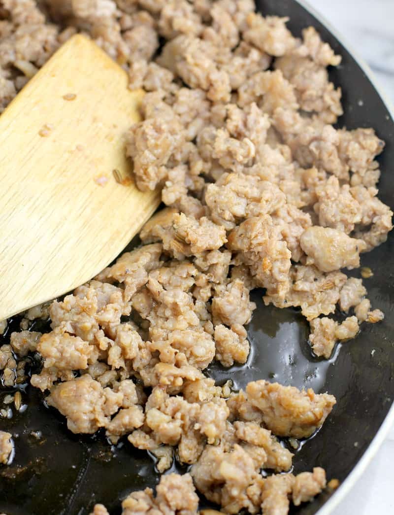 juicy browned sausage (one of the ingredients for lasagna) in a skillet with a wooden spatula