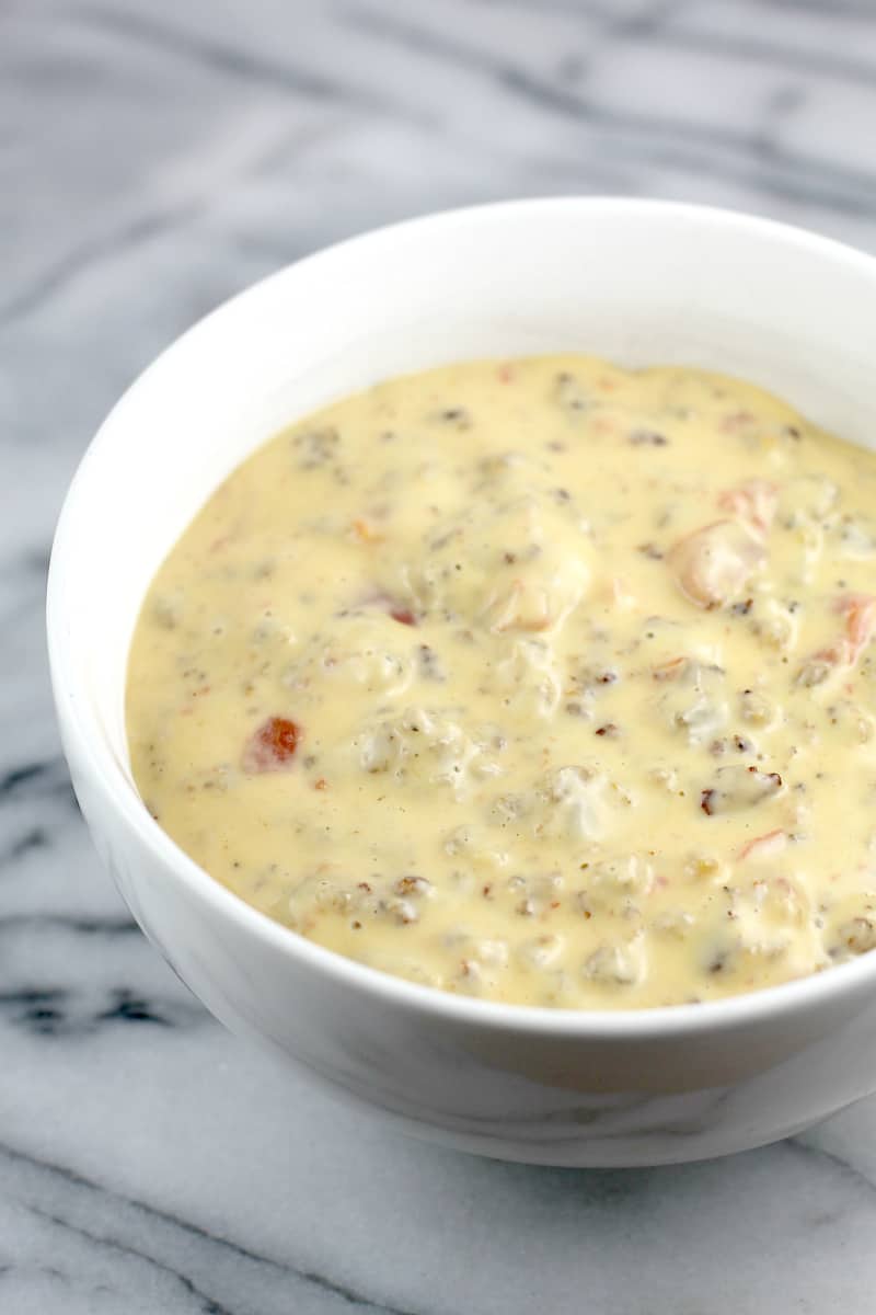 Side view of white bowl on marble surface, full of finished queso