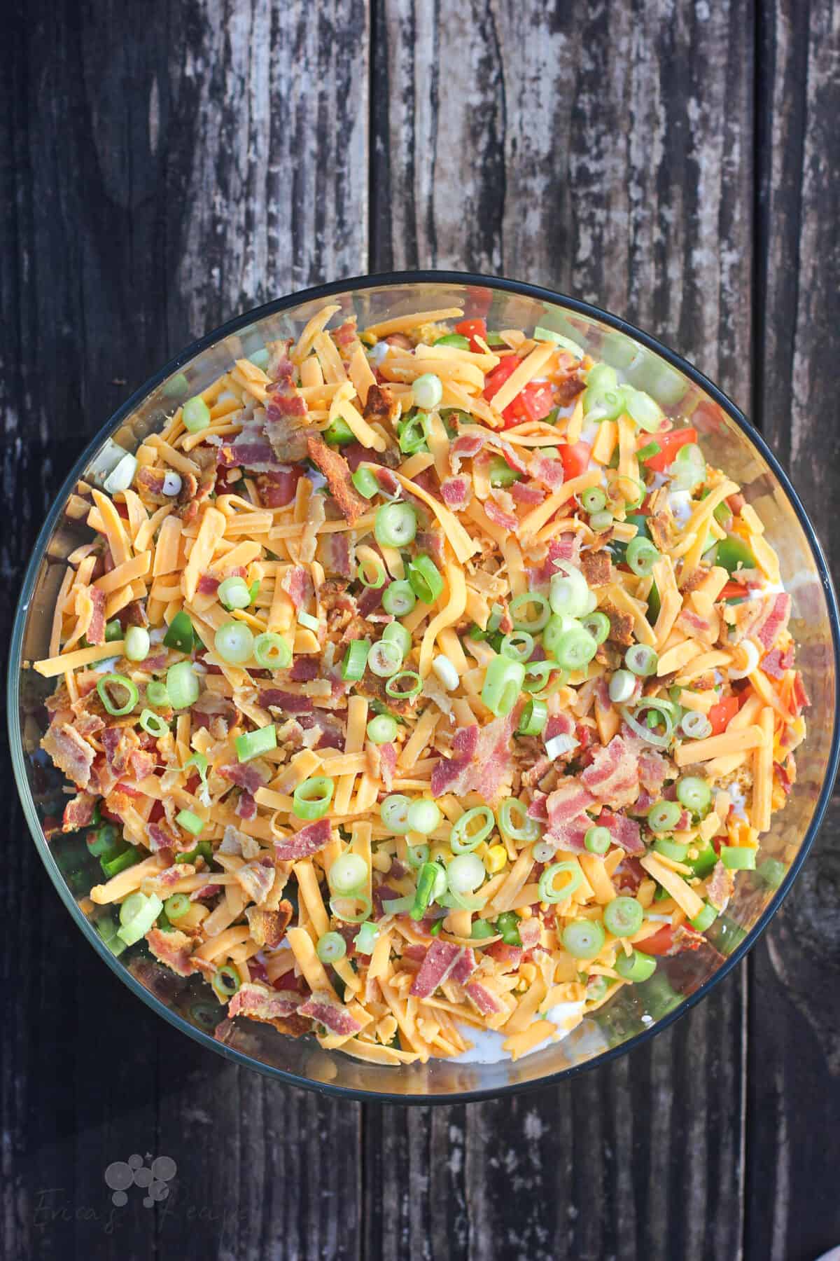 bowl of cornbread salad in clear glass bowl on weather wood table