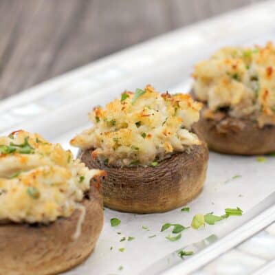 three crab stuffed mushrooms on a piece of white parchment on a silver serving plate