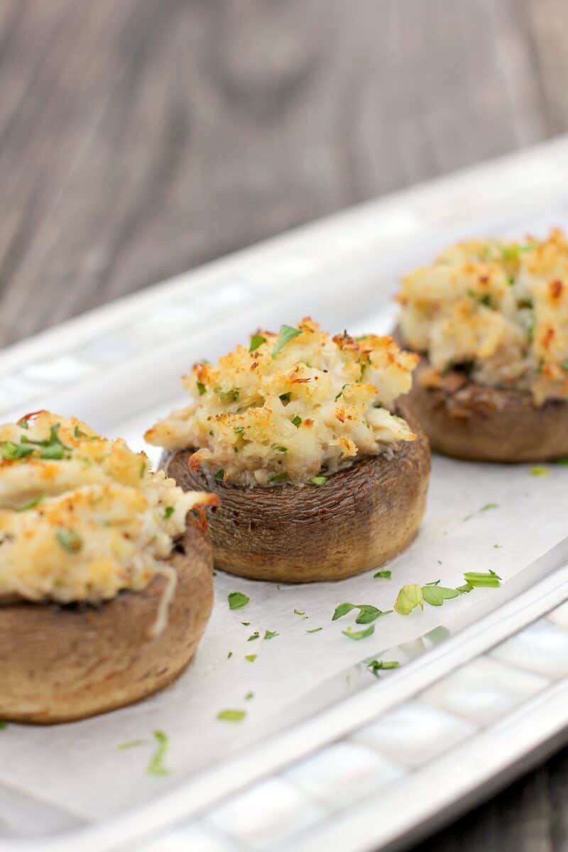 three crab stuffed mushrooms on a piece of white parchment on a silver serving plate