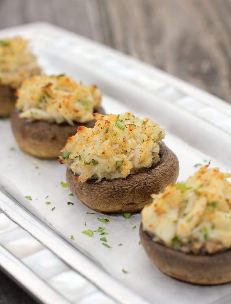 four stuffed mushrooms with crab in a row on serving plate