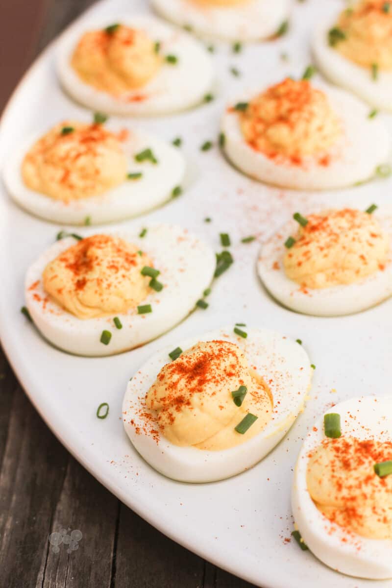 prepared deviled eggs topped with chives on a white serving platter