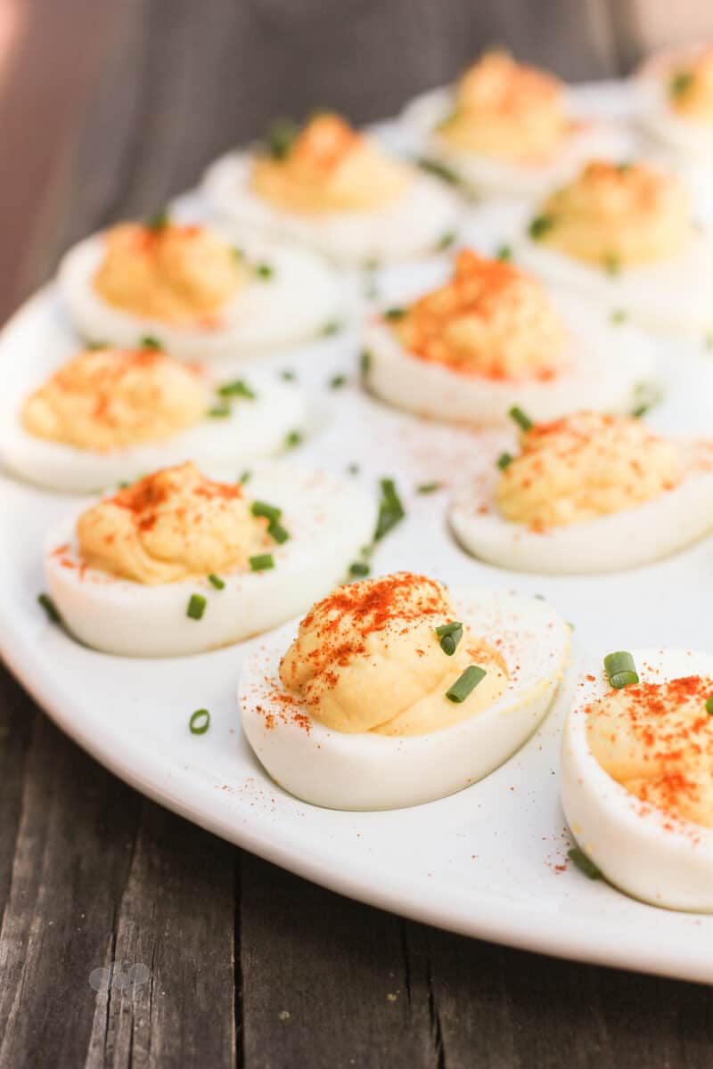 side view deviled eggs topped with chives on a white serving platter