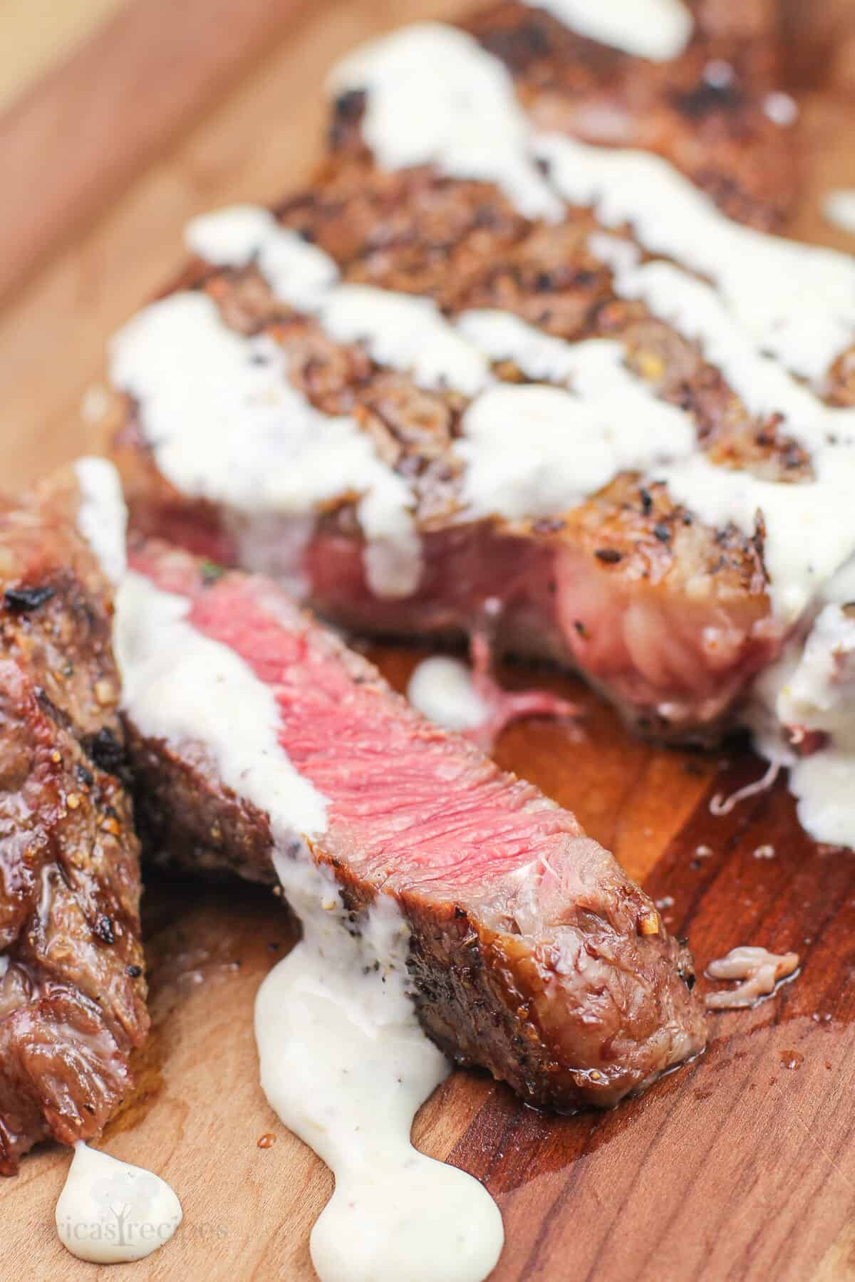 cut steak on wood board topped with horseradish mustard sauce