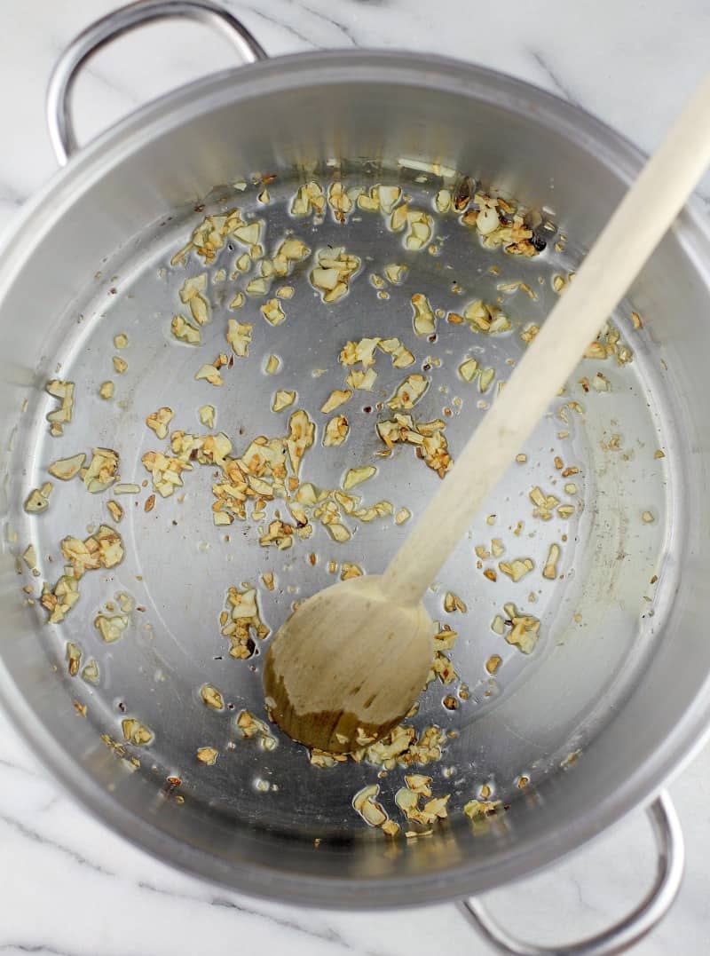 Top down view into a pot with a wooden spoon to show the browned garlic cooking