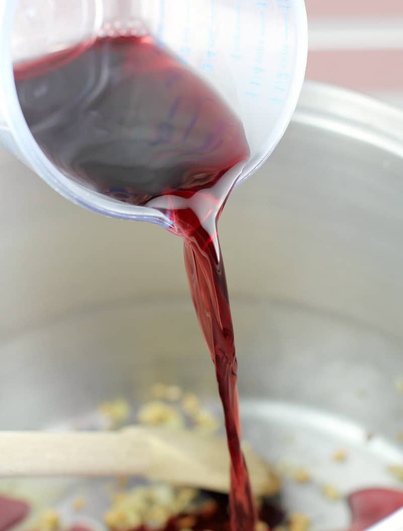 Clear plastic measuring cup pouring red wine into the pot