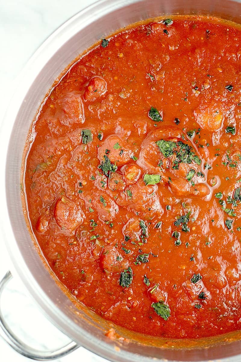 Top down view into the pot to show the finished canned tomatoes sauce; fresh herb is sprinkled on top