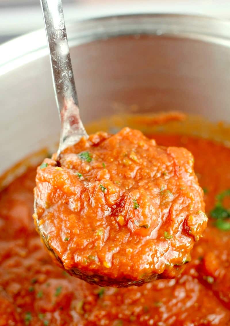 Ladle holding up finished marinara sauce out of a pot