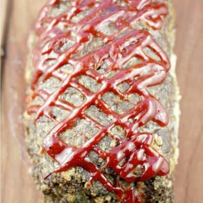 whole cooked best meatloaf ever on a wood board showing the criss-cross ketchup mixture on top