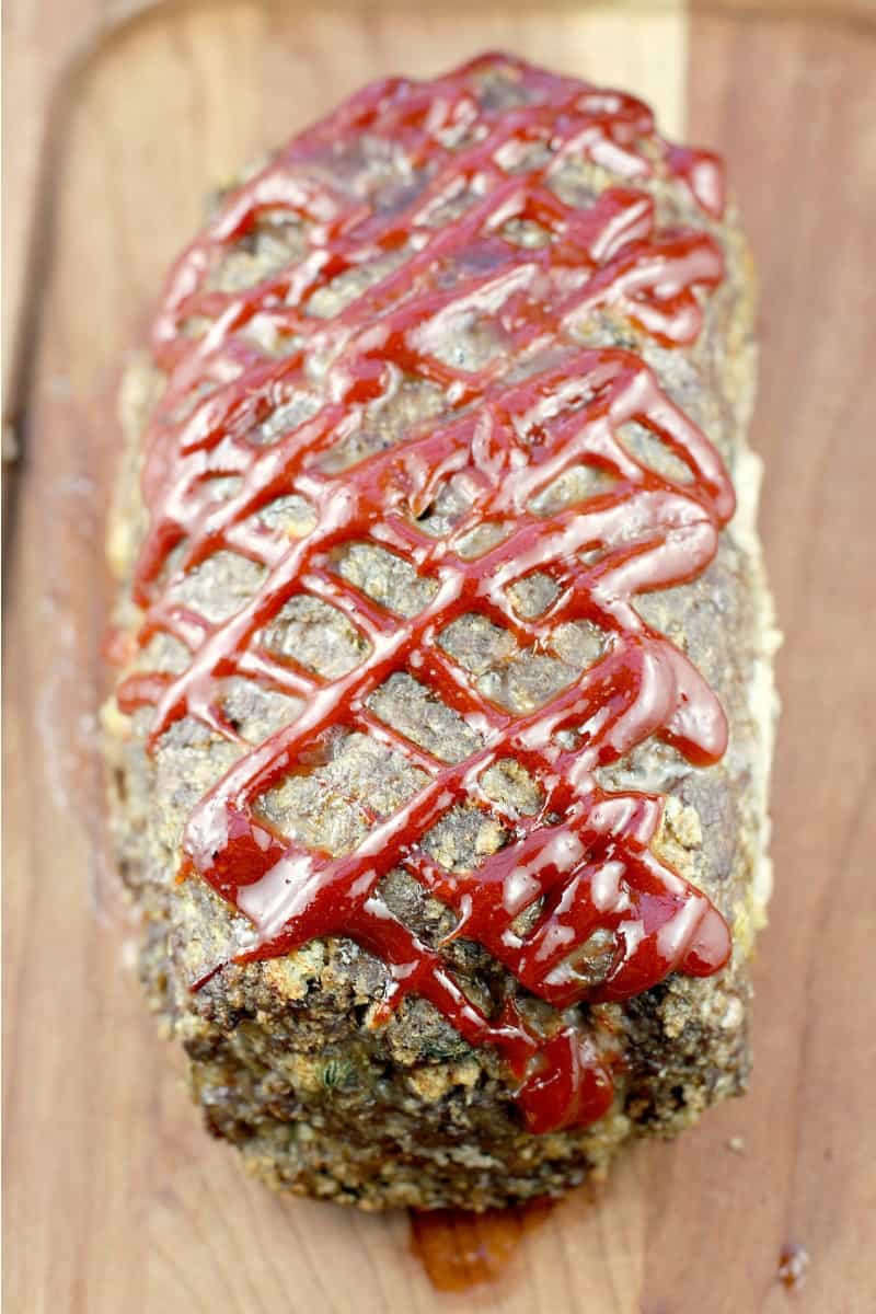 whole cooked best meatloaf ever on a wood board showing the criss-cross ketchup mixture on top