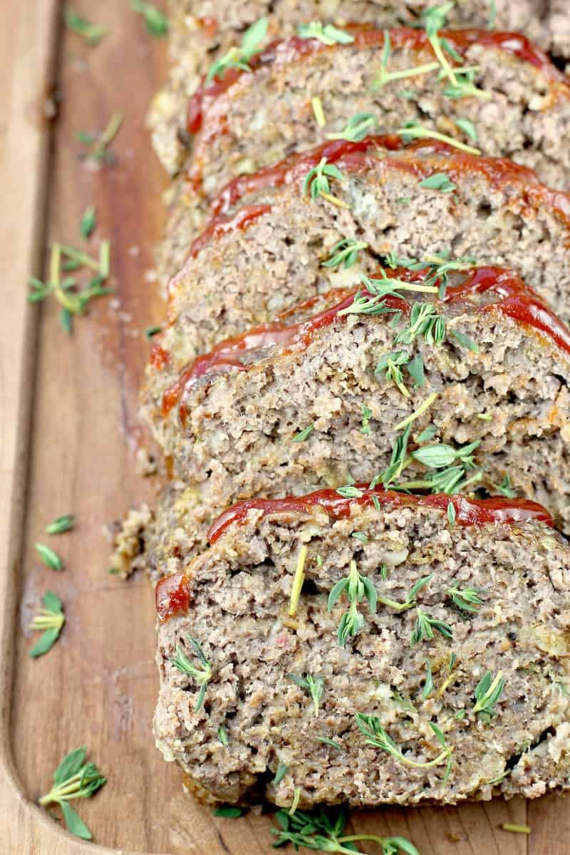 close up of the sliced meatloaf on a wood board, thyme sprinkled over