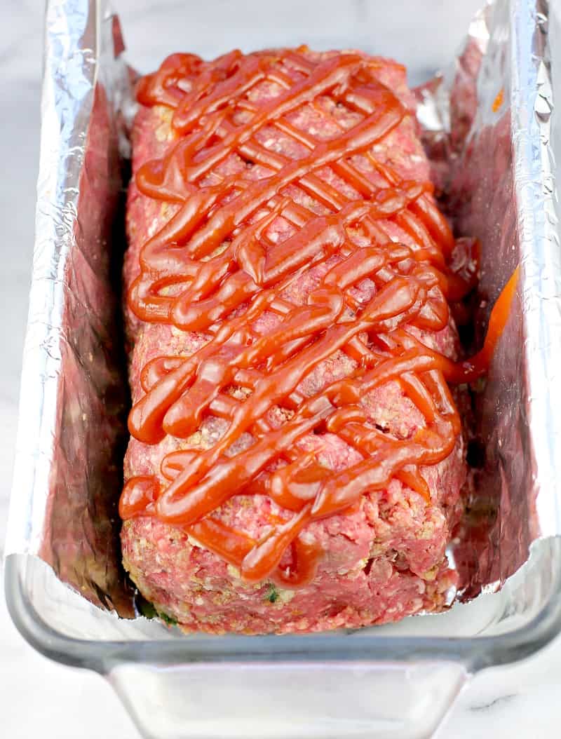 the prepared meatloaf topped with the ketchup mixture in a clear glass loaf pan lined with foil