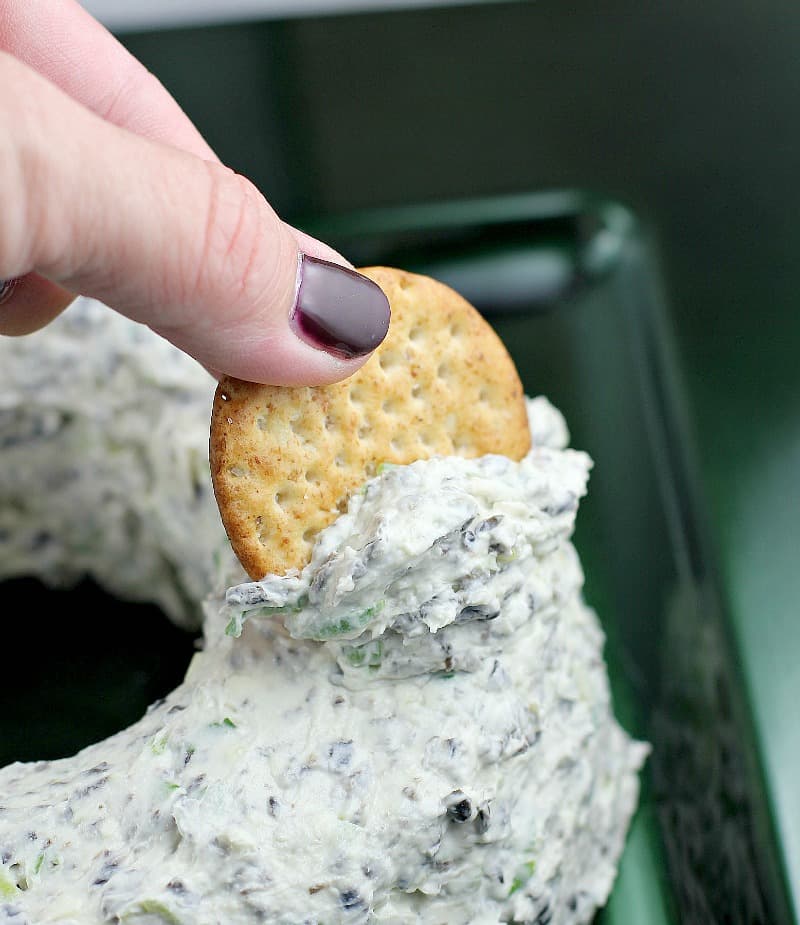 side view showing a person scooping up dip from the side of the cheese wreath