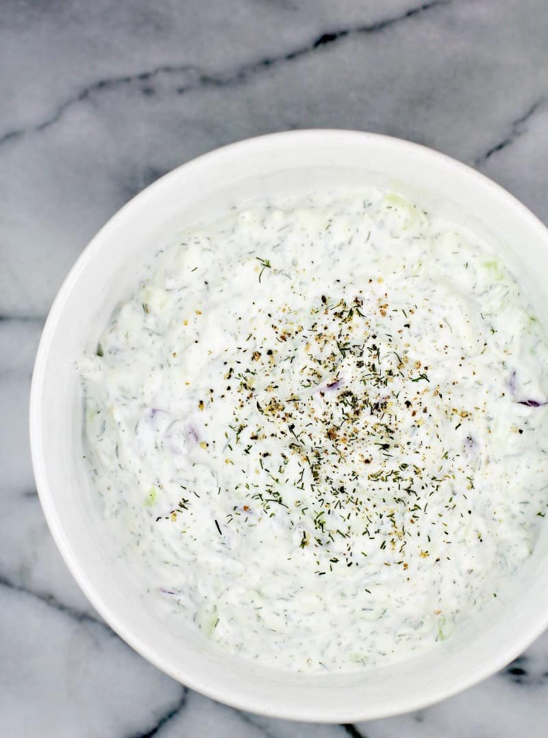 top down view of the healthy veggie dip tzatziki with sour cream in a white ceramic bowl; the sauce is topped with fresh cracked pepper