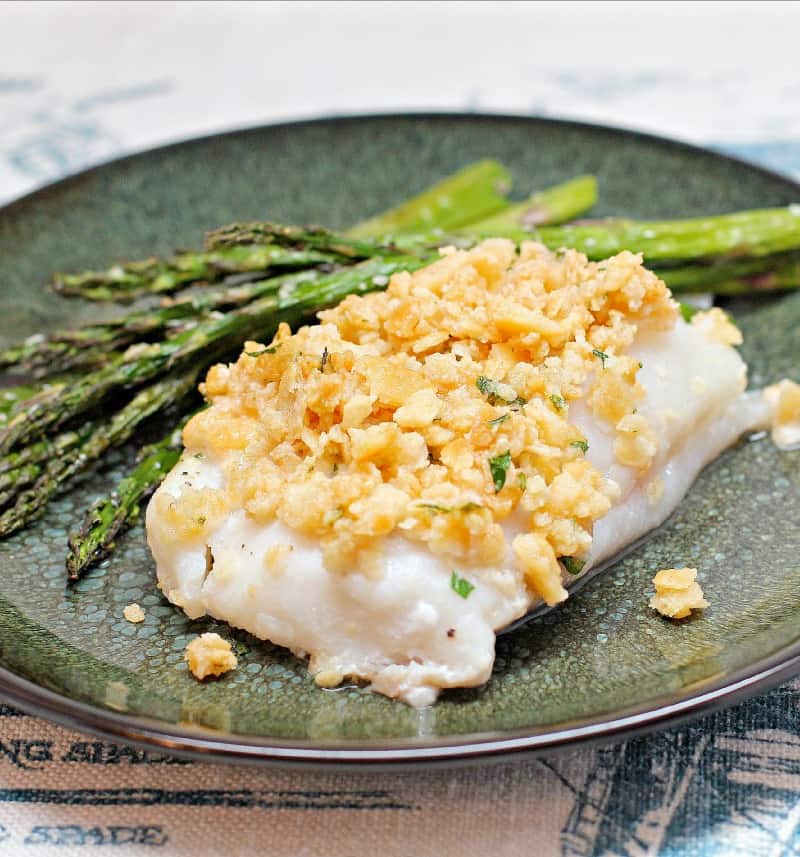 cooked fish topped with cracker stuffing on a green plate with asparagus