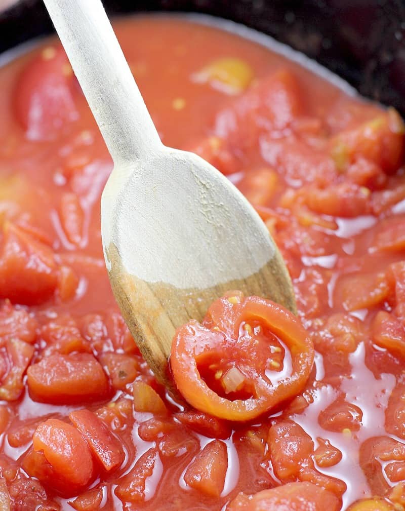 wooden spoon breaking up the stewed tomatoes