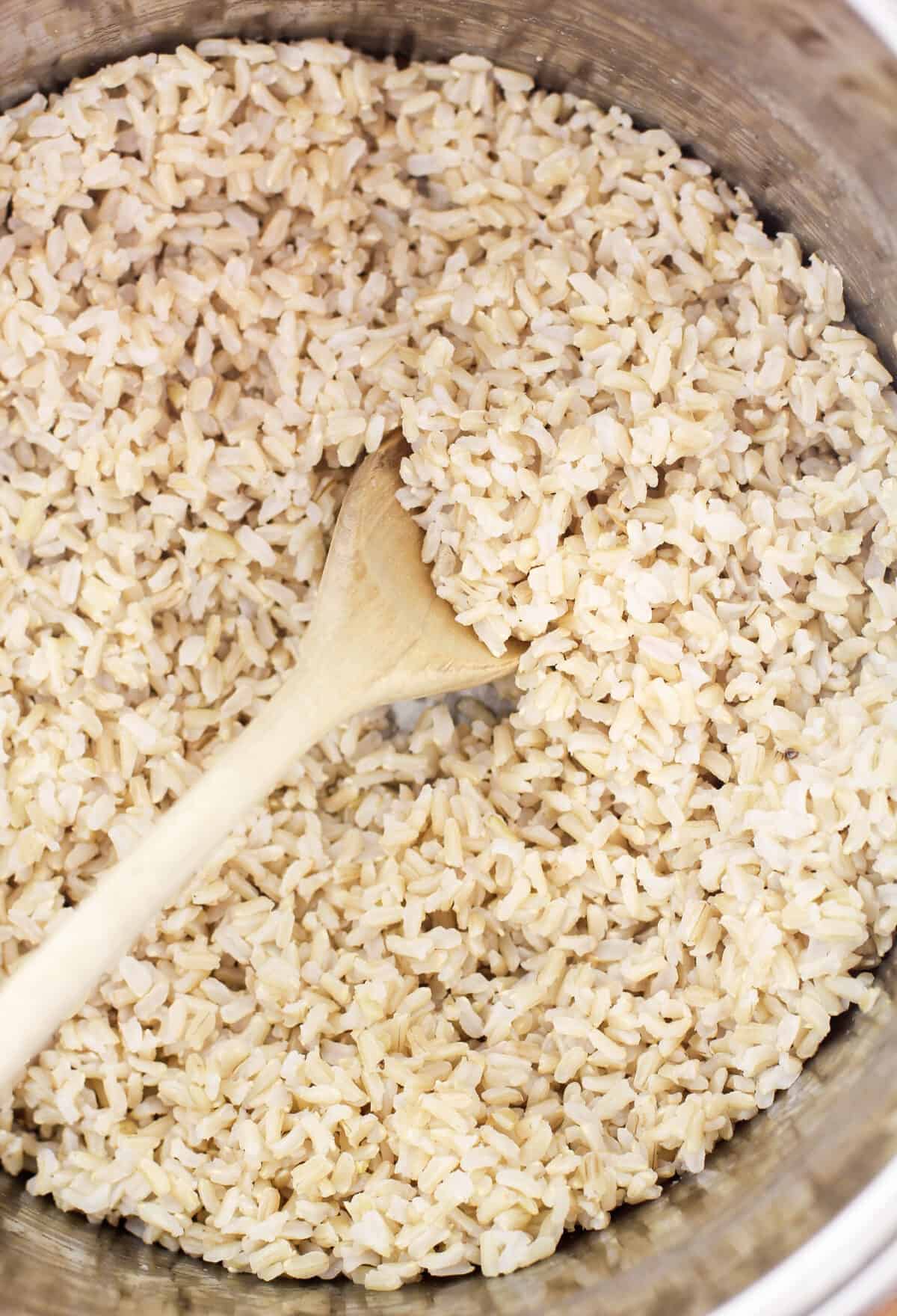 cooked brown rice in pot with wood spoon