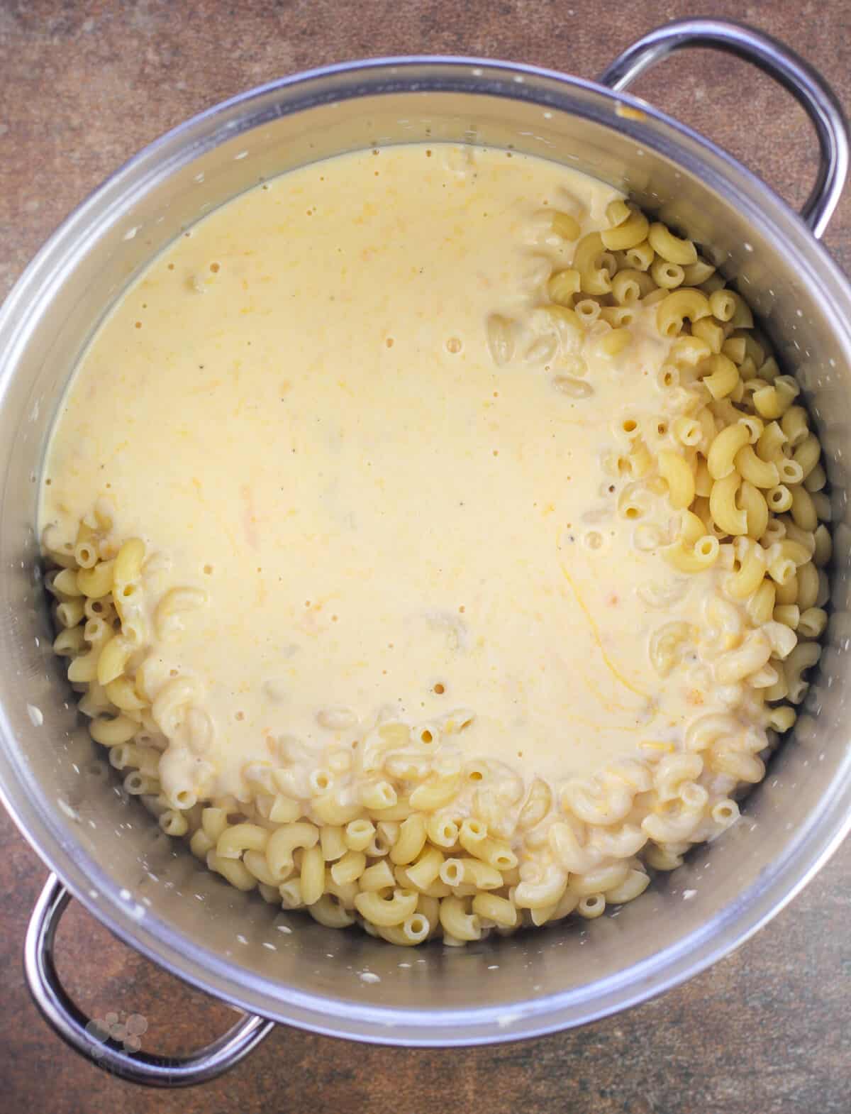 cheese sauce added to macaroni in metal pot