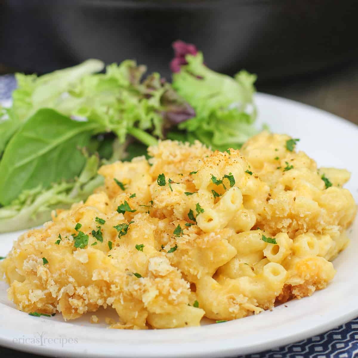 simple creamy macaroni and cheese on white plate with salad; cast iron skillet in background