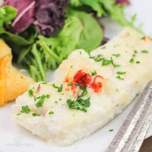 portion of prepared haddock with lobster sauce on white plate with salad and roll