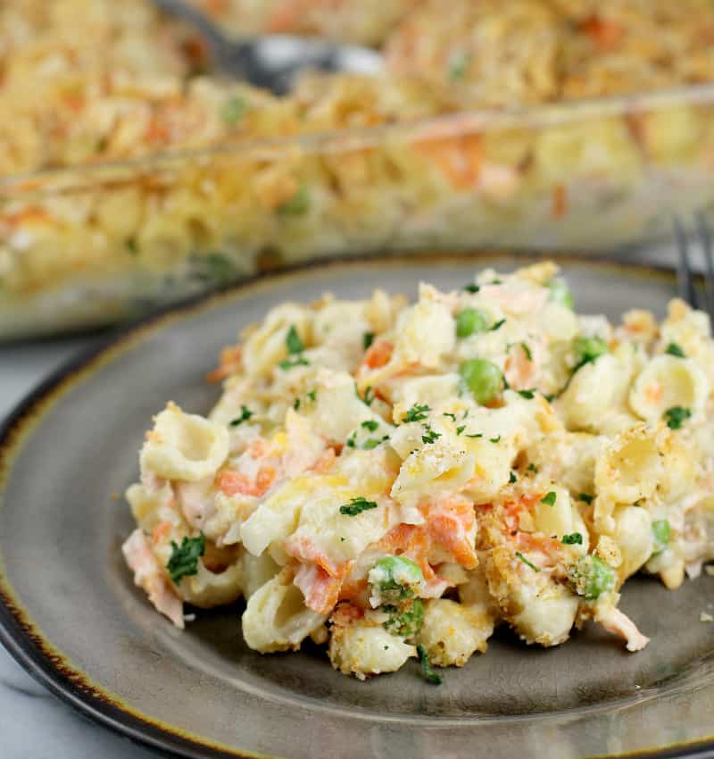 cooked salmon casserole on a serving plate in the foreground, rest of casserole in a bake dish in the background