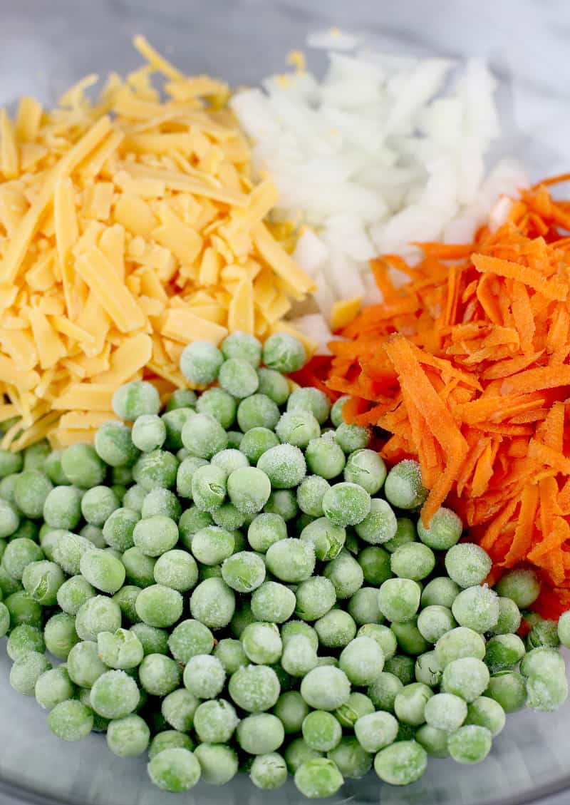 peas, shredded cheese, diced onion, and shredded carrot in a bowl