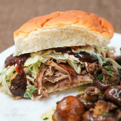 a pulled pork sandwich with cole slaw and bbq sauce on white plate with mushrooms.