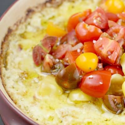 baked green chili artichoke dip in a red ceramic dish topped with tomatoes and olive oil