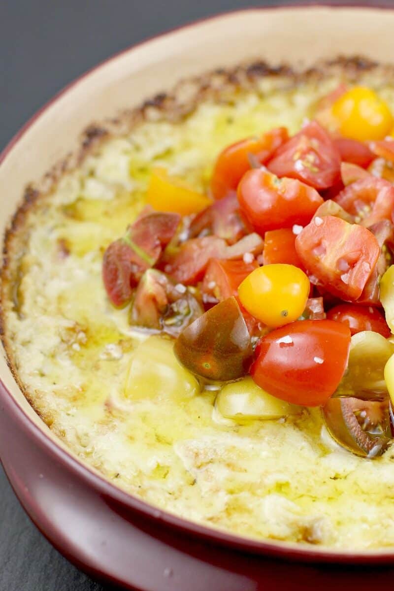 baked green chili artichoke dip in a red ceramic dish topped with tomatoes and olive oil