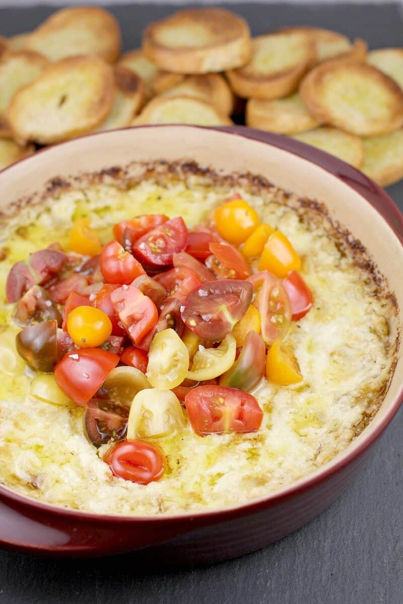 baked artichoke dip in bake dish with crostini in the background