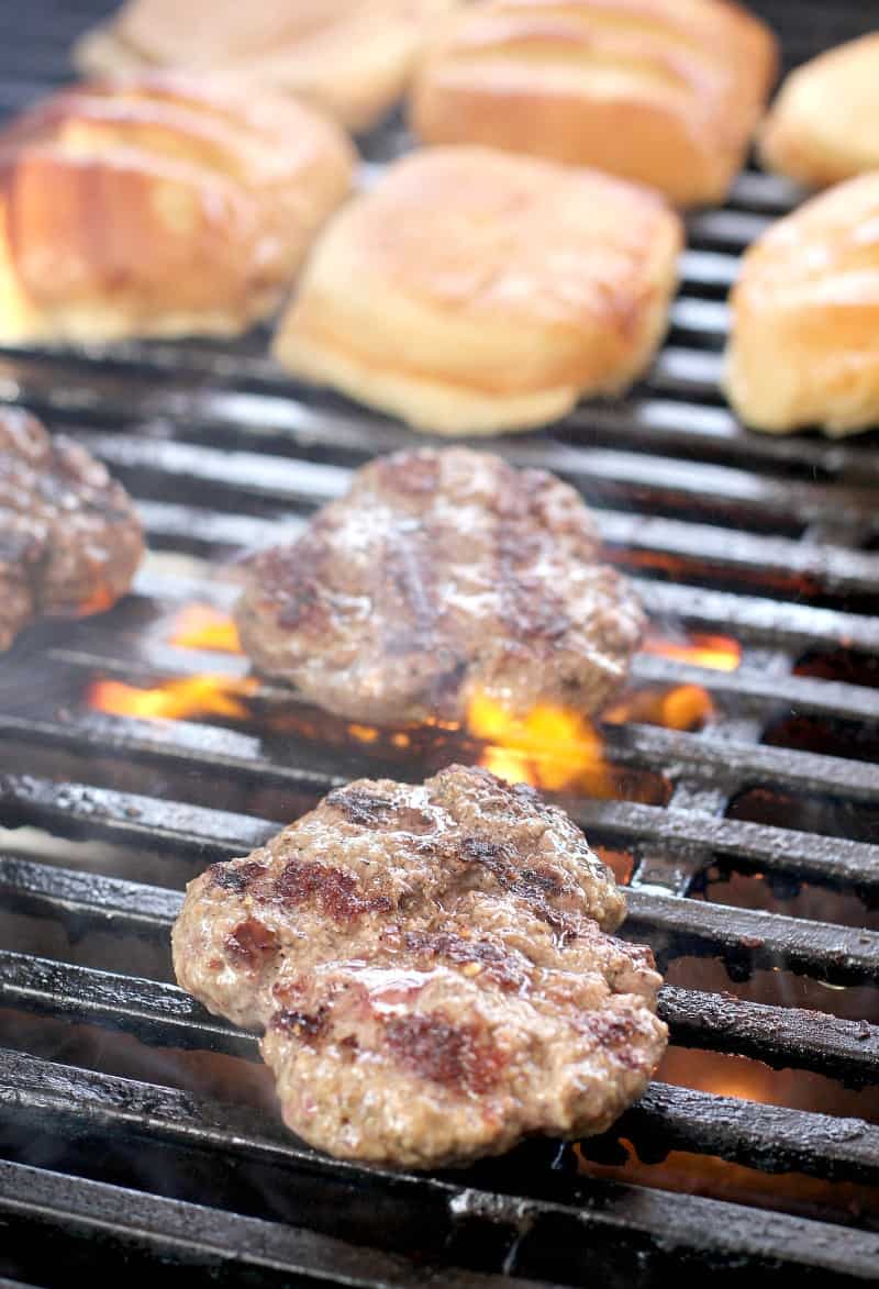 hamburgers cooking on a grill, buns toasting in the background