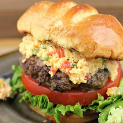 close view of assembled jalapeno pimento cheese burger on a plate, sliced jalapeno on the side