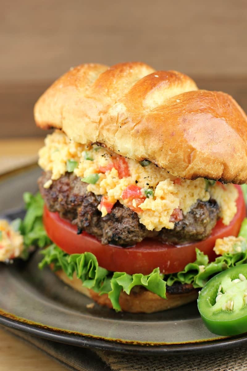 close view of assembled jalapeno pimento cheese burger on a plate, sliced jalapeno on the side