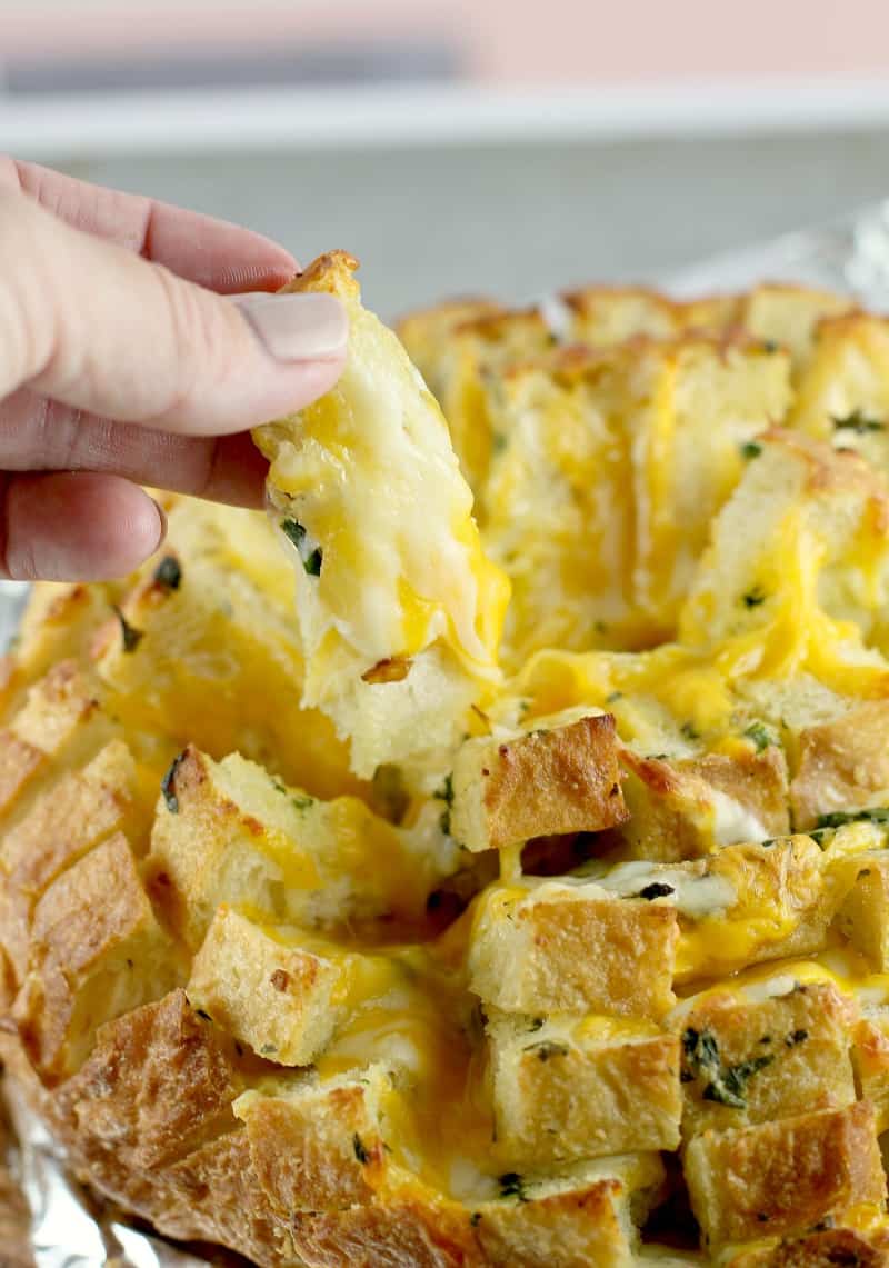 side view of a hand lifting up a piece of the garlic herb and cheese pull apart bread to show the cheesiness