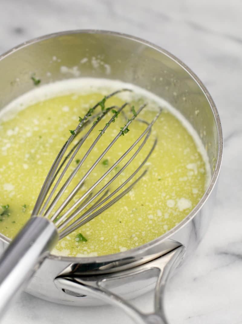 a small steel saucepan with a whisk on marble. in the saucepan is the butter garlic mixture