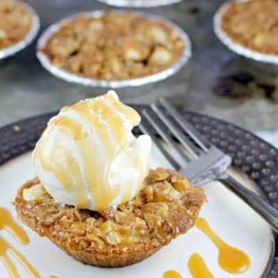 mini apple crisp pie on a plate topped with ice cream and caramel drizzled over, fork on the side