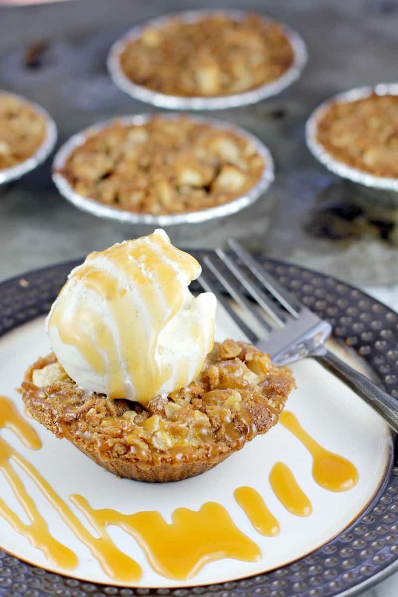 mini apple crisp pie on a plate topped with ice cream and caramel drizzled over, fork on the side