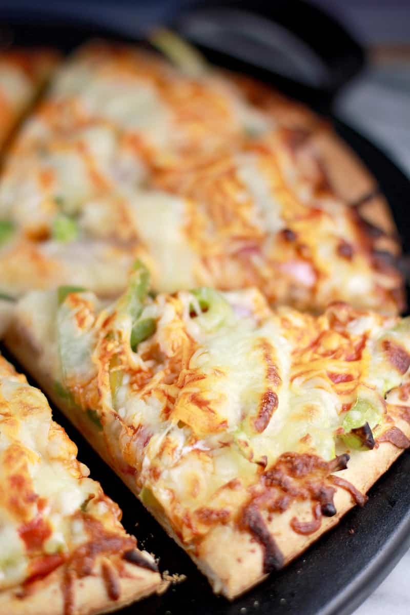 Top down/side angle from the right; the cooked buffalo turkey pizza on a black pizza stone surface, sliced into individual slices.