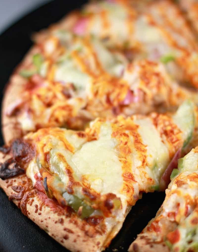 Top down/side angle from the left; the cooked buffalo turkey pizza on a black pizza stone surface, sliced into individual slices.