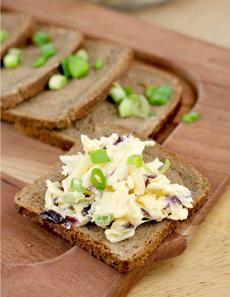 brown bread squares on a cutting board; in the foreground, one bread piece has Russian Garlic cheese on it