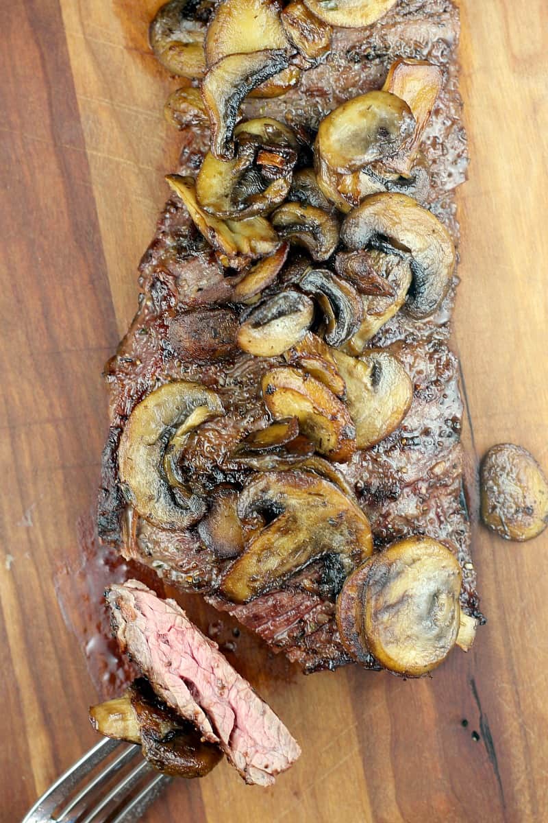 top down view of cooked steak on wood board with fork holding cut piece