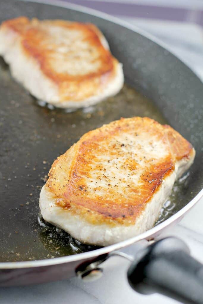 pork chop searing in a skillet to show browning